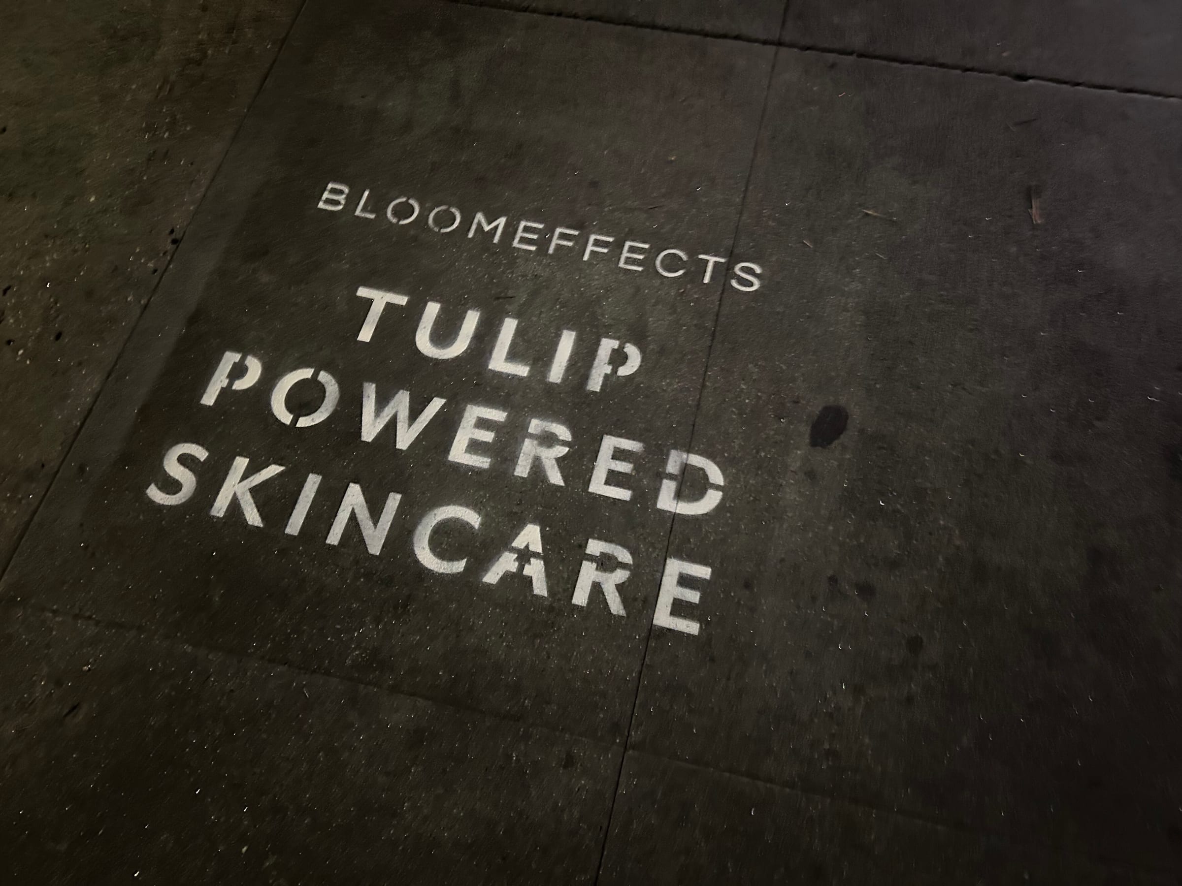 Sidewalk stencil install for Bloomeffects 'Tulip Powered Skincare' on New York City sidewalk in New York City — white stencil with tulip flower mark on concrete by Beyond Street Media