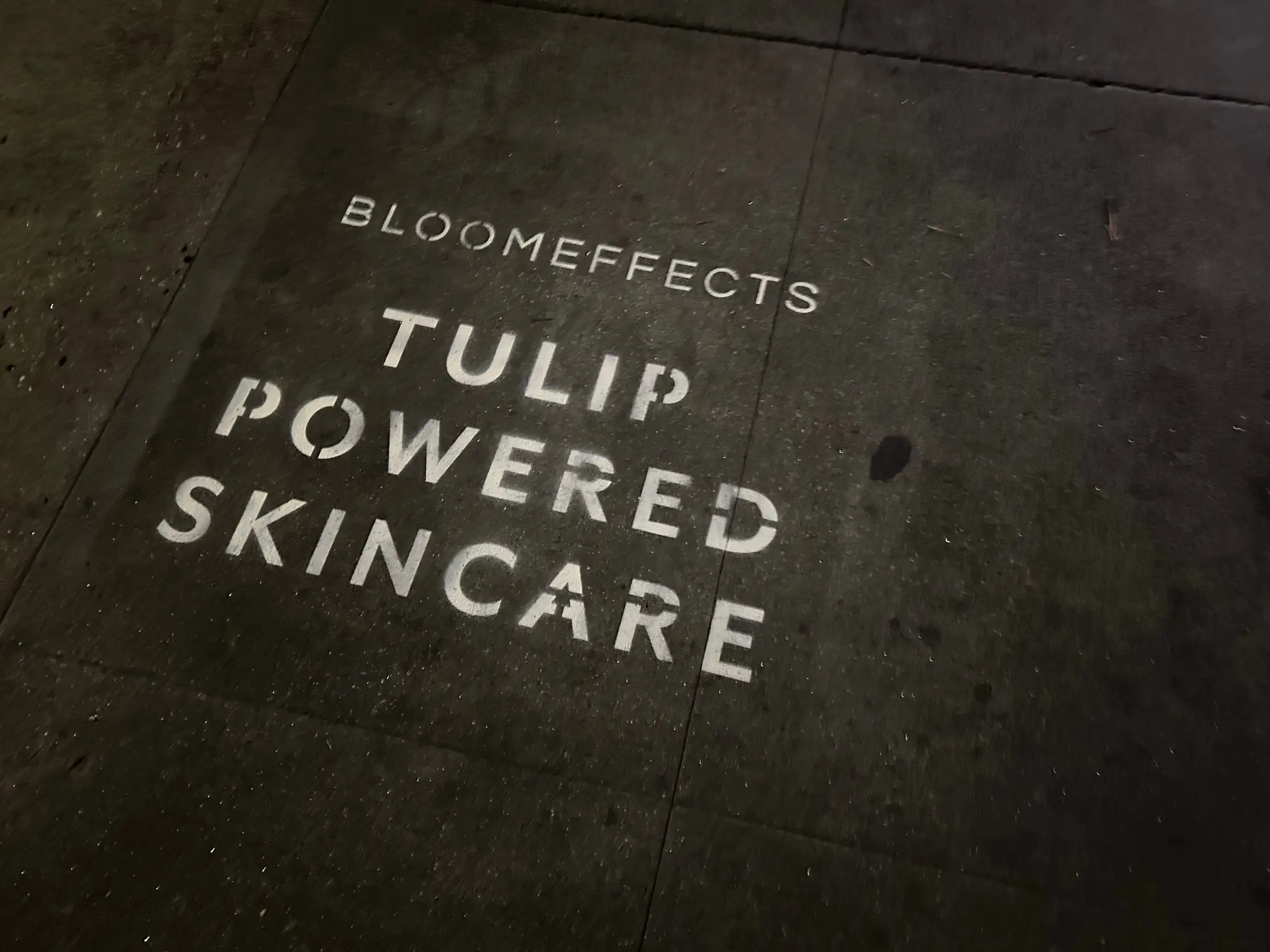 Sidewalk stencil install for Bloomeffects 'Tulip Powered Skincare' on New York City sidewalk in New York City - white stencil with tulip flower mark on concrete by Beyond Street Media