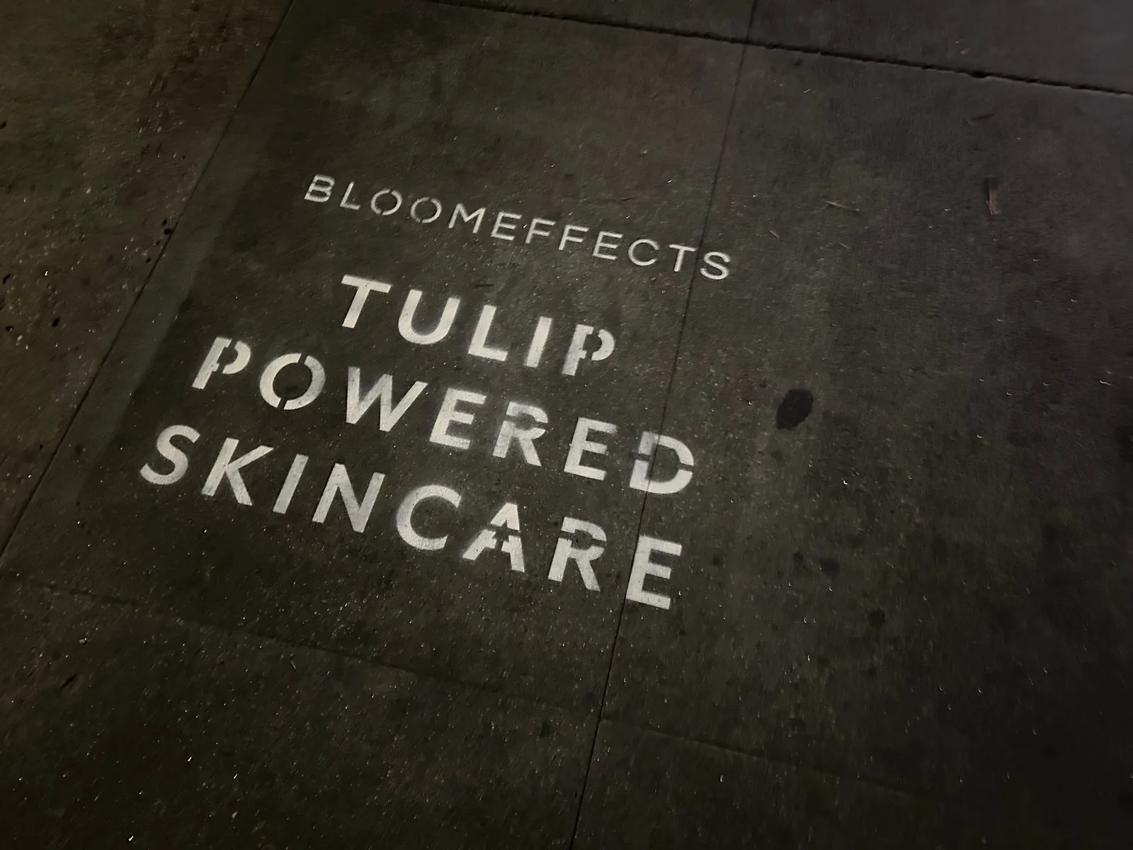 Sidewalk stencil install for Bloomeffects 'Tulip Powered Skincare' on New York City sidewalk in New York City - white stencil with tulip flower mark on concrete by Beyond Street Media