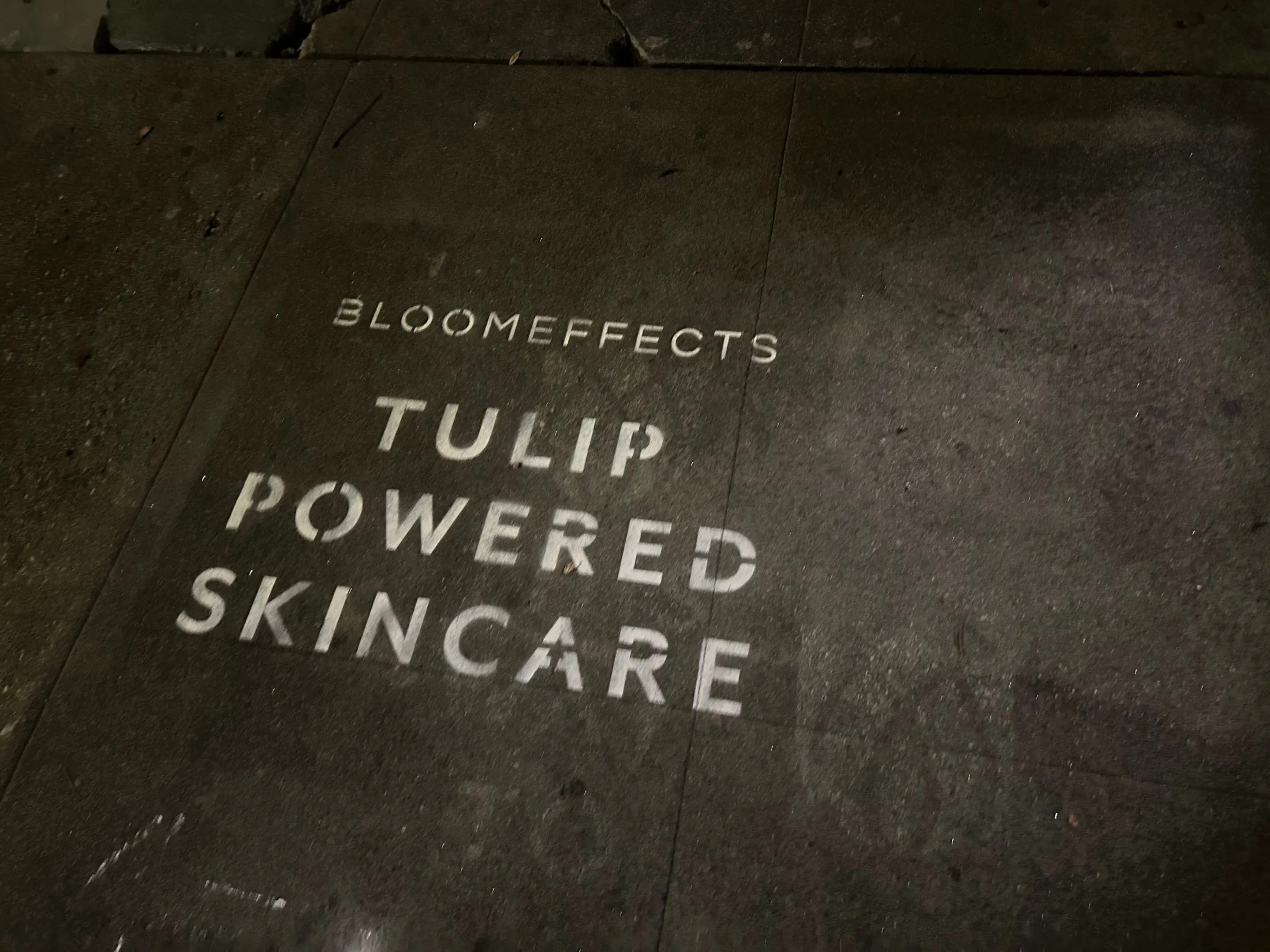 Sidewalk stencil install for Bloomeffects 'Tulip Powered Skincare' on New York City sidewalk in New York City - white stencil with tulip flower mark on concrete by Beyond Street Media