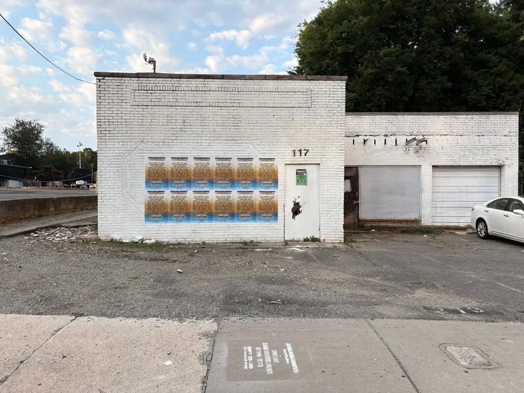 Grid of Breakaway Music Festival posters wheatpasted on a white brick building, E 9th St, Charlotte