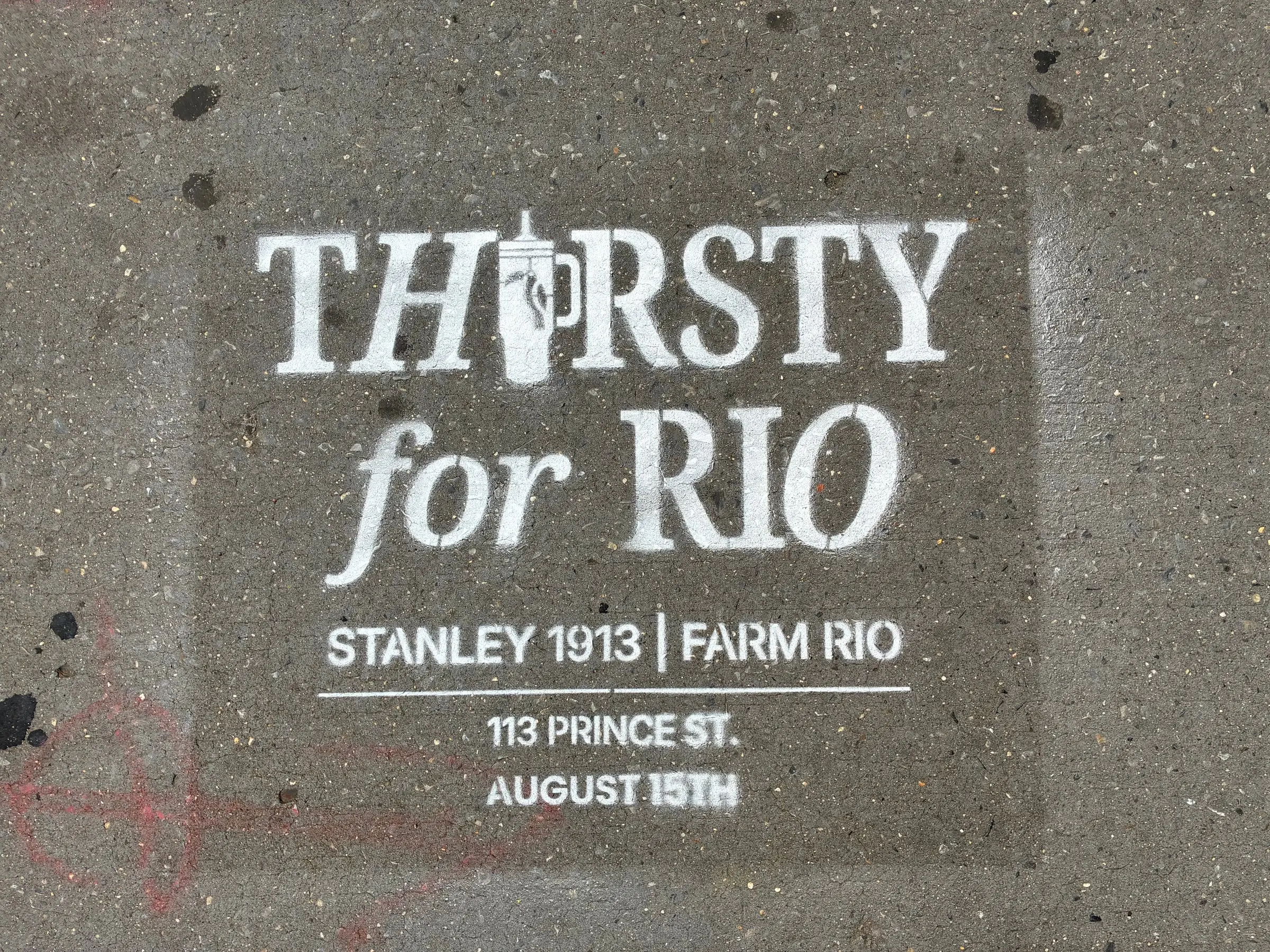 Close-up of the Thirsty for Rio chalk stencil with the Stanley tumbler standing in as the I, pointing to 113 Prince St in SoHo.