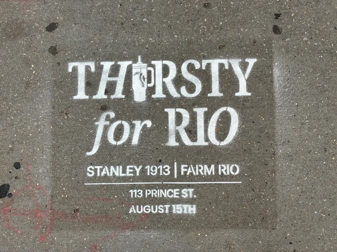 Close-up of the Thirsty for Rio chalk stencil with the Stanley tumbler standing in as the I, pointing to 113 Prince St in SoHo.