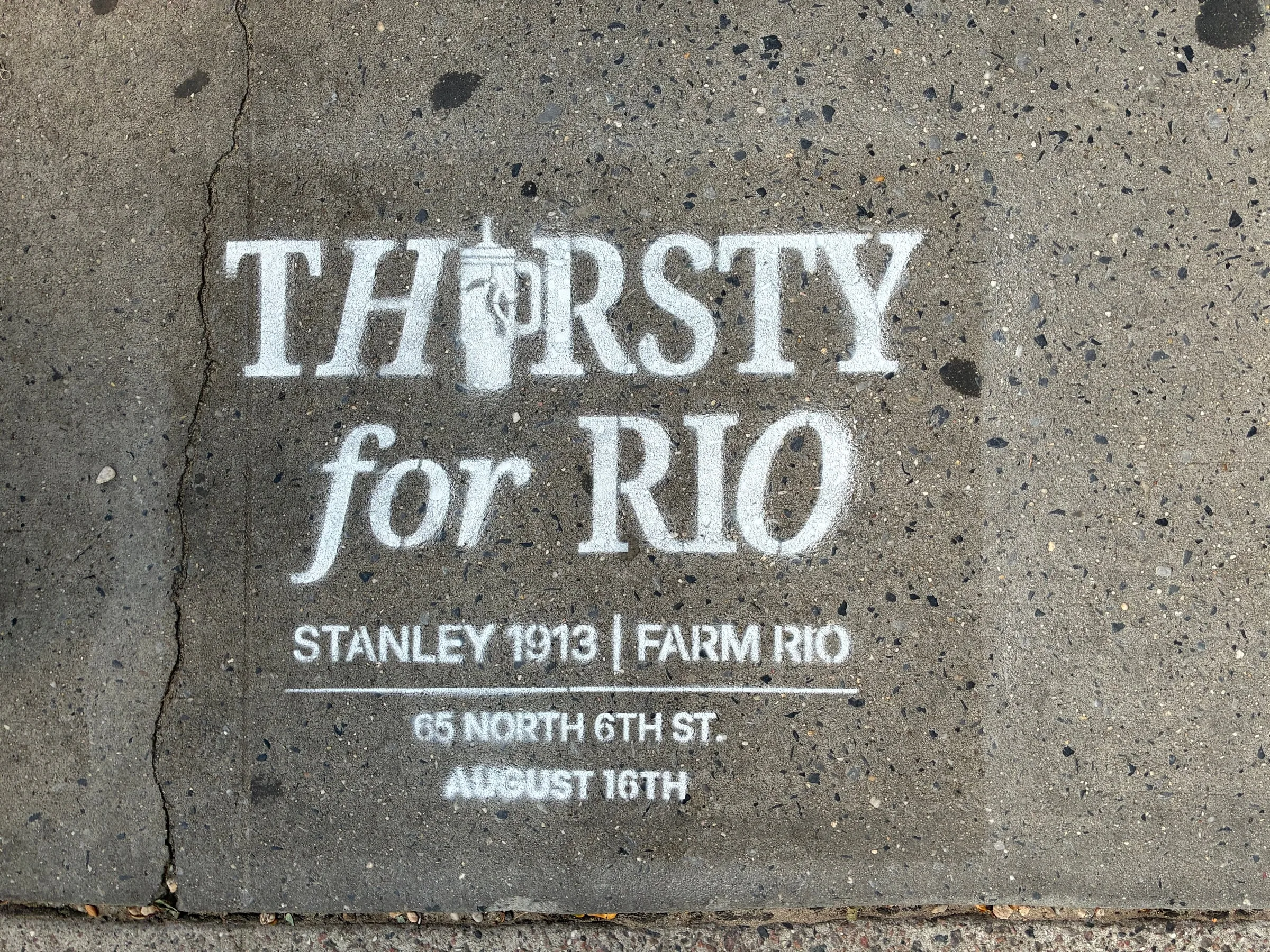 Thirsty for Rio stencil head-on on Williamsburg concrete, directing to the 65 North 6th St store event.