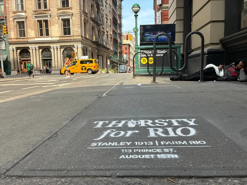 Thirsty for Rio stencil in front of the Prince St subway entrance in SoHo with a taxi passing beyond.