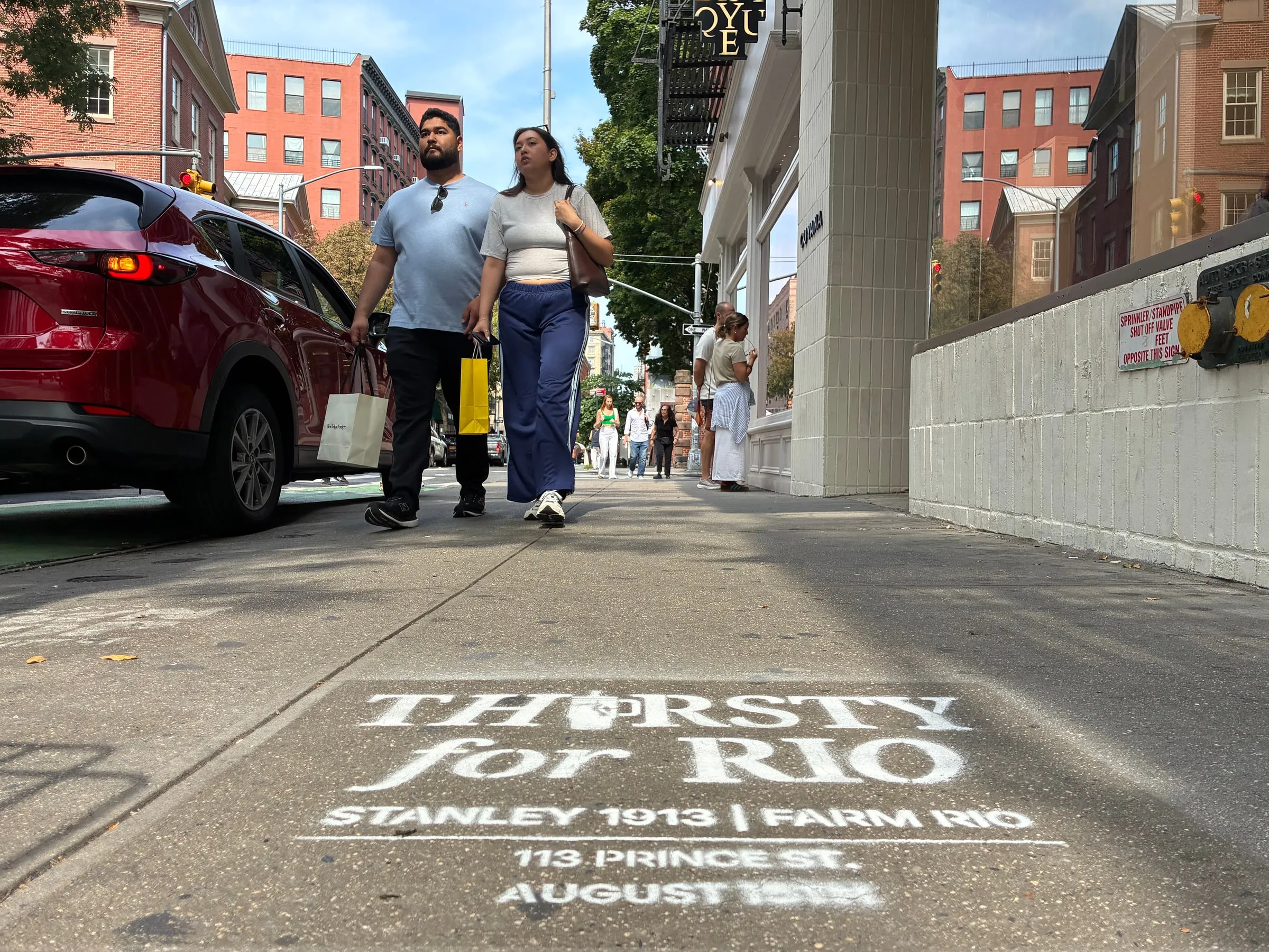 Two shoppers walking past the Thirsty for Rio stencil on the Prince St approach in SoHo.
