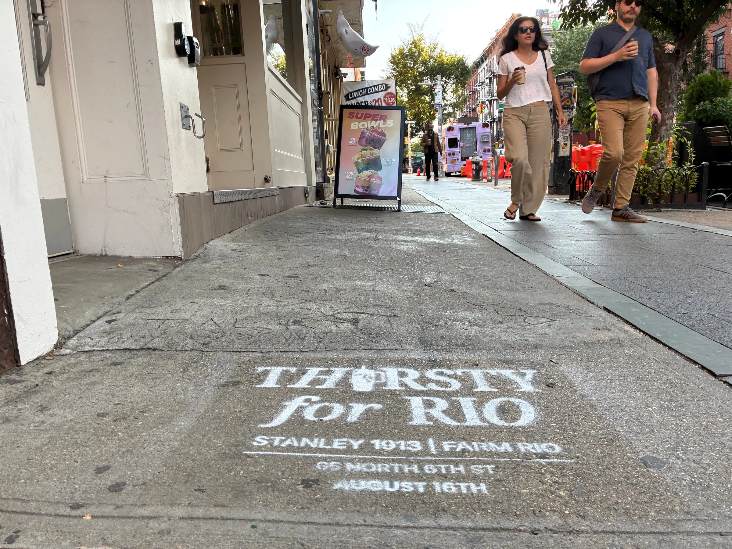 Farm Rio x Stanley 1913 chalk stencil reading Thirsty for Rio on the North 6th St sidewalk in Williamsburg, pedestrians and cafe signage beyond.