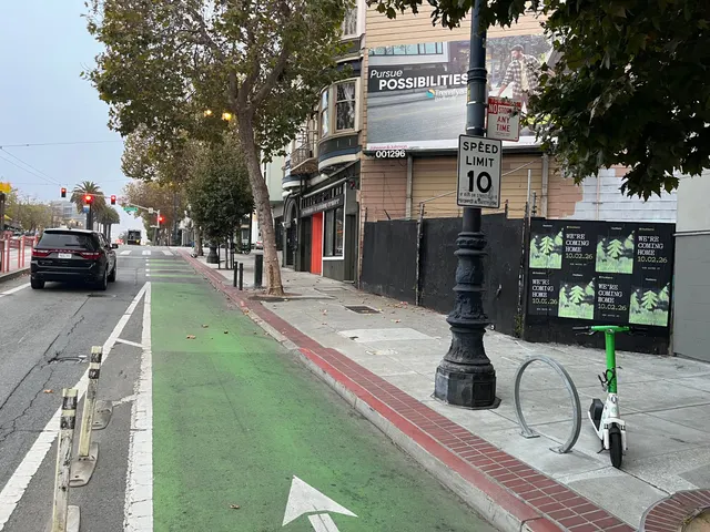 Huckberry wheatpaste posters on a black fence on Market Street near Octavia, on the Mission side, a lamppost and scooter in front, looking down the bike lane