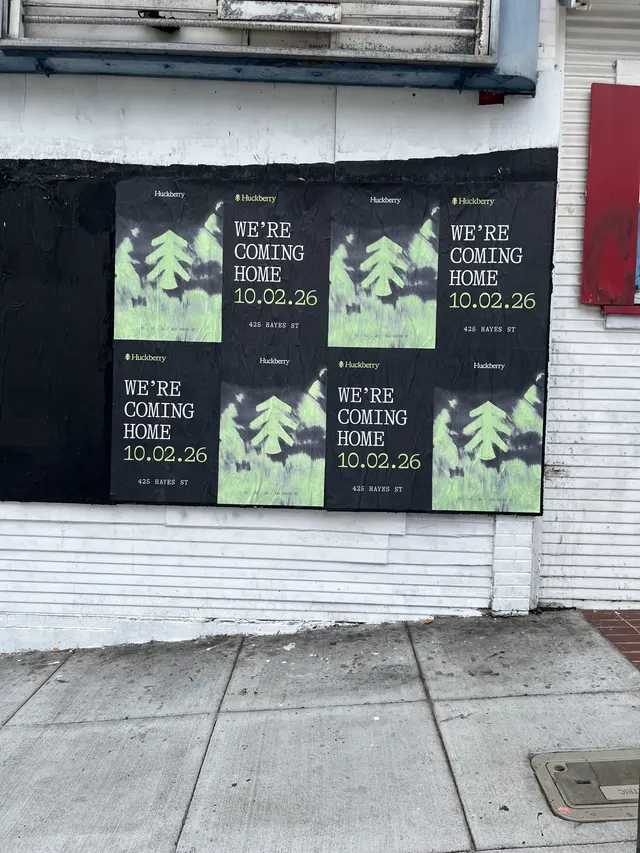 Huckberry wheatpaste posters on a white clapboard wall at Octavia and Market, the two designs alternating, close up