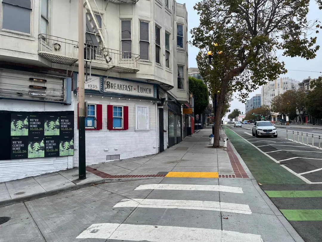 Huckberry wheatpaste posters on a white corner building at Octavia and Market, a crosswalk and the green bike lane in front