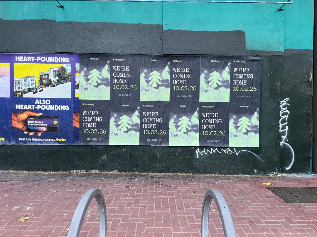 Huckberry wheatpaste posters, twelve sheets in two rows of six, on a teal and black wall on Market Street between Gough and Octavia, beside other posters