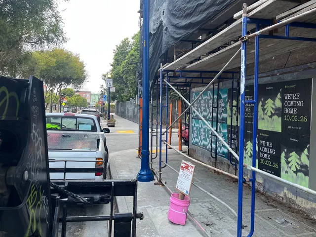 Huckberry wheatpaste posters on boards along a scaffolded sidewalk at Oak Street and Octavia Boulevard, Hayes Valley
