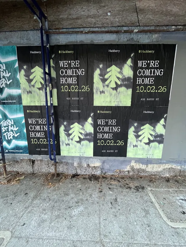 Huckberry wheatpaste posters stacked in a narrow bay behind scaffolding at Oak Street and Octavia Boulevard, Hayes Valley, close up