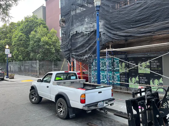 Huckberry wheatpaste posters behind scaffolding and black netting at Oak Street and Octavia Boulevard, Hayes Valley, a pickup at the curb