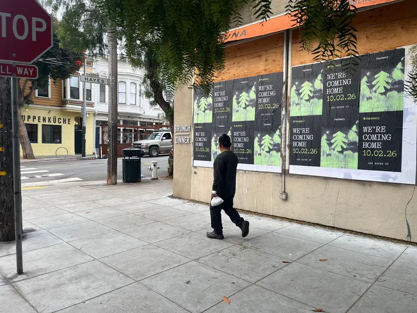 Huckberry wheatpaste posters on a boarded corner storefront at Hayes and Laguna, Hayes Valley, a pedestrian walking past and the 600 Hayes street sign across the street