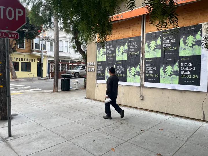 Huckberry wheatpaste posters on a boarded corner storefront at Hayes and Laguna, Hayes Valley, a pedestrian walking past and the 600 Hayes street sign across the street