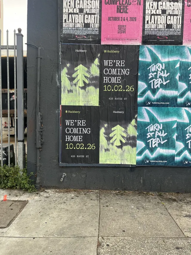 Huckberry wheatpaste posters among other event posters on a black wall on Bryant Street near 10th, SoMa, close up