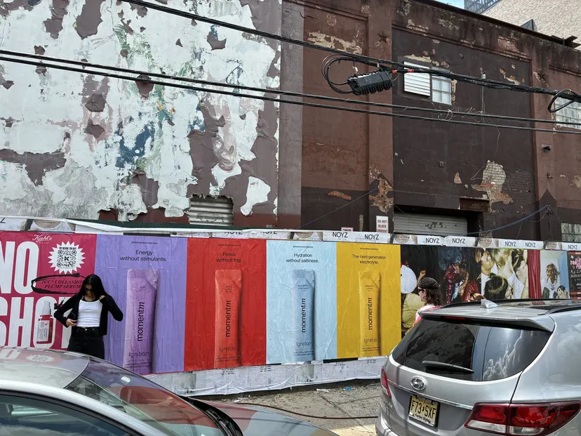 Dense Momentm poster wall on a Williamsburg, Brooklyn street with parked cars passing.