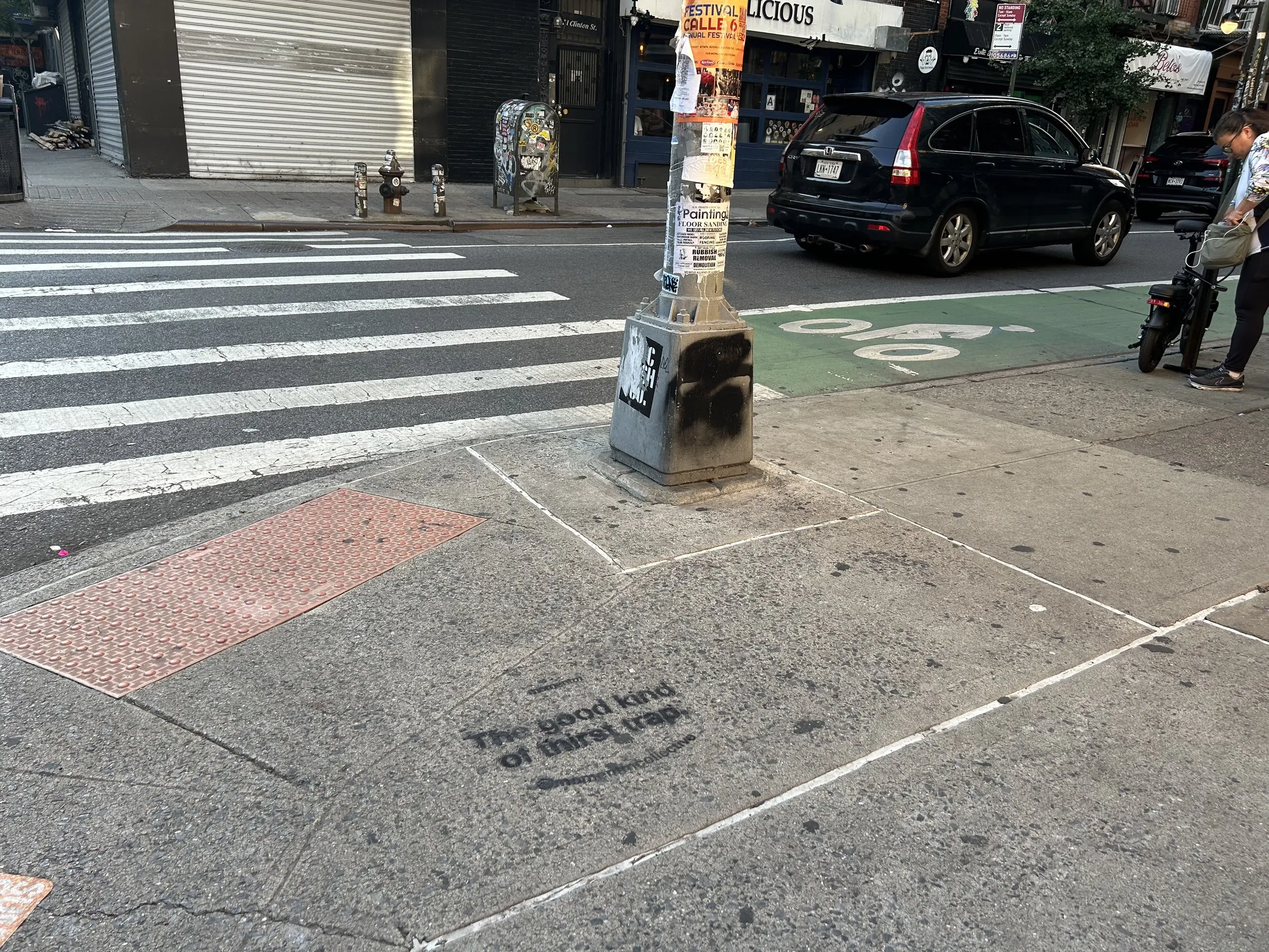 White Momentm stencil at a crosswalk corner, matched to the dark pavement per the two-tone install spec.