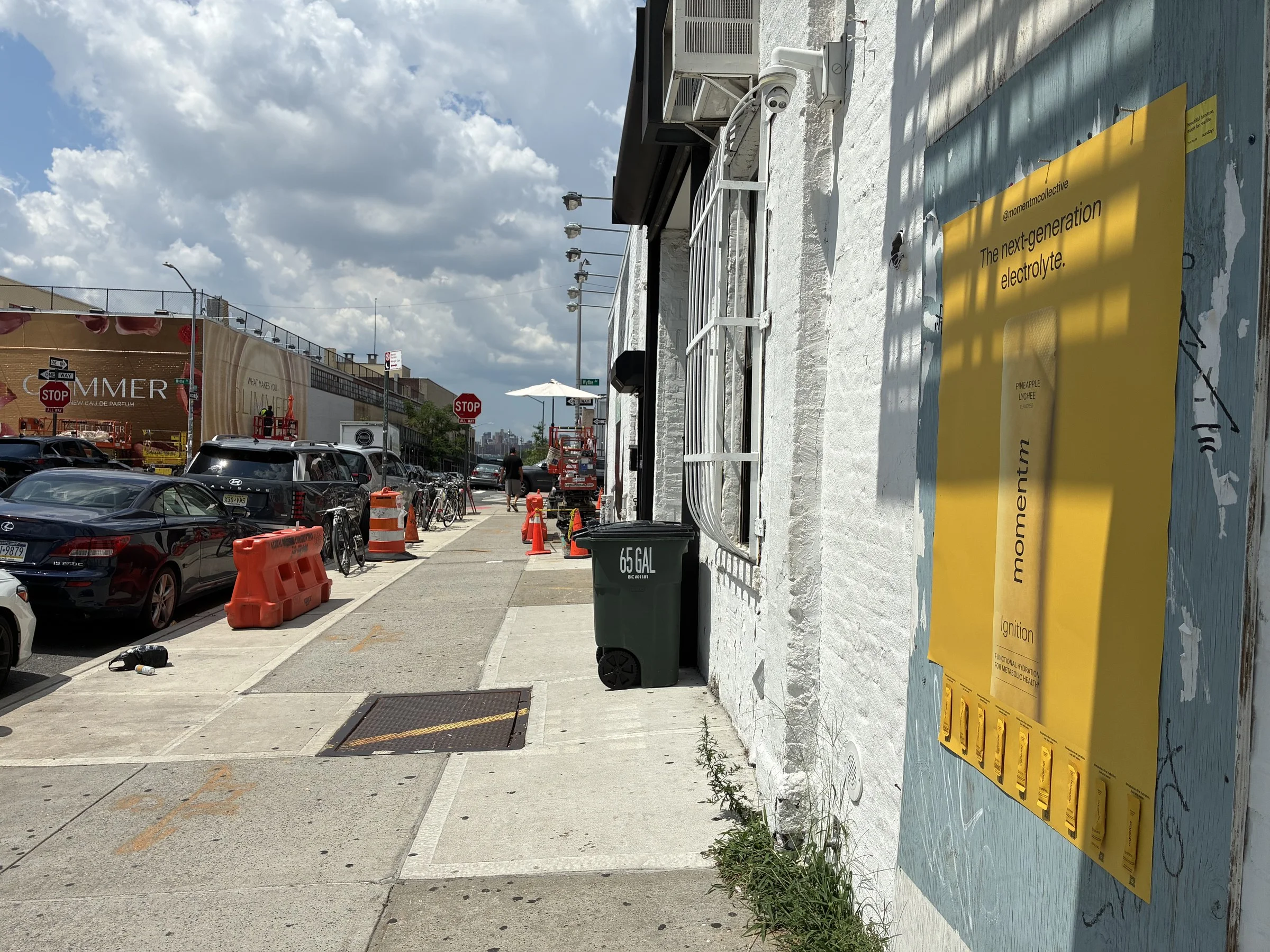Angled view of the yellow Momentm takeaway poster with sample stick packs, Williamsburg street beyond.