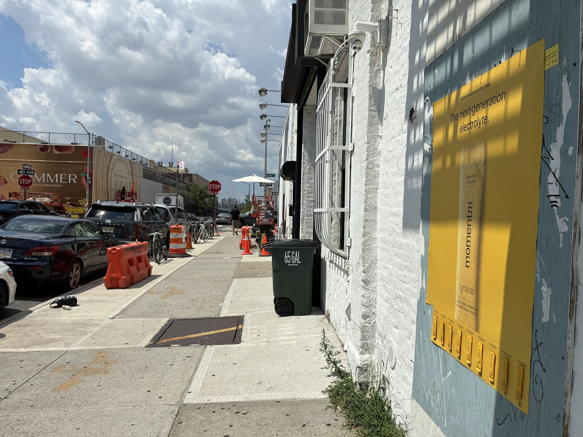 Angled view of the yellow Momentm takeaway poster with sample stick packs, Williamsburg street beyond.