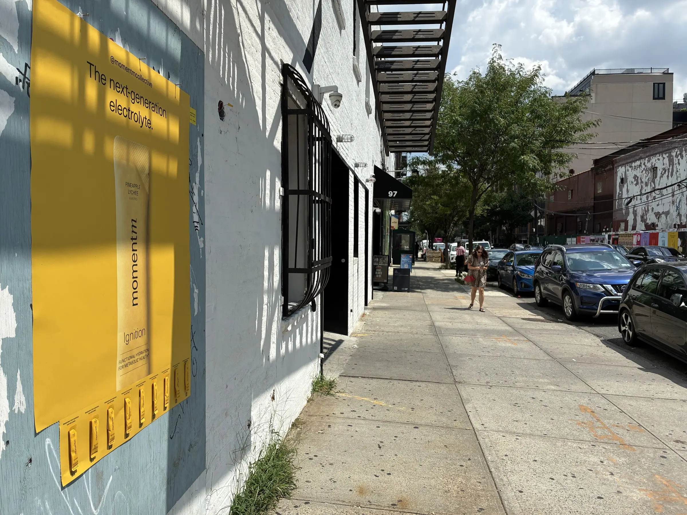 Momentm 48x36 takeaway poster with attached samples on a painted brick wall in Williamsburg, Brooklyn.