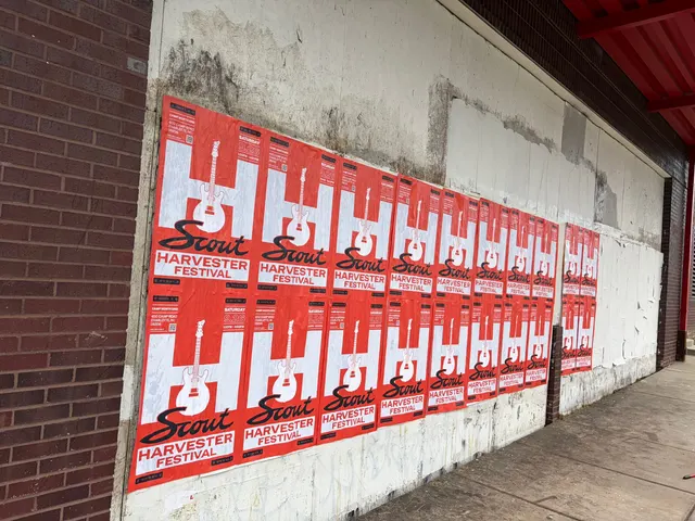 Scout Harvester wheatpaste in the red-orange colorway on a grimy white wall under a red steel eave, East 11th Street, First Ward