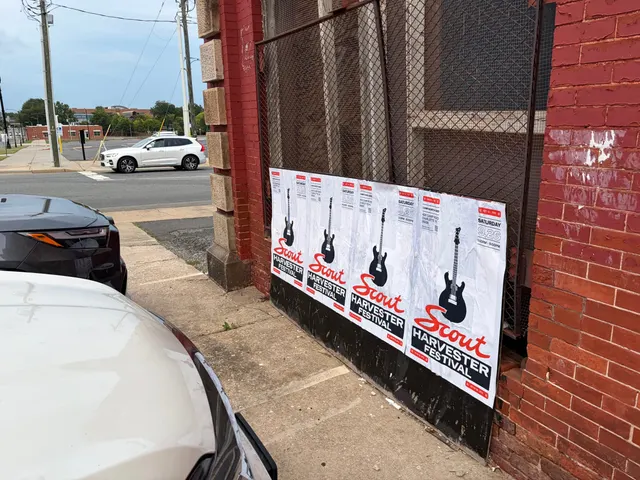 Scout Harvester wheatpaste in the white and silver colorway on a mesh-covered wall at North Brevard Street, a sports car at the curb