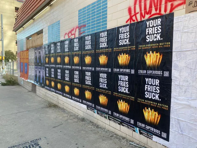 Stolon Superfoods wheatpaste posters at a raking angle, receding under red graffiti tags, on Lavaca Street at 16th, in daylight