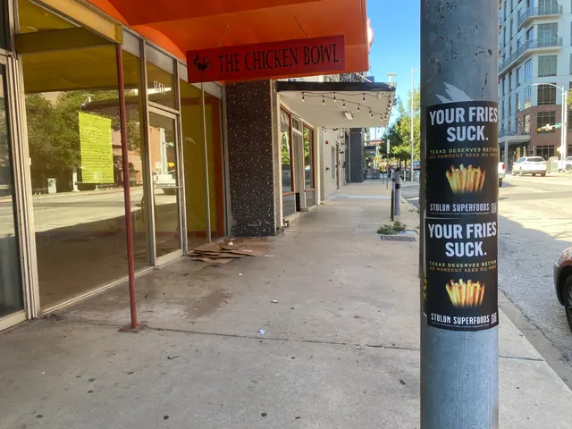 Stolon Superfoods pole stickers, two YOUR FRIES SUCK. snipes stacked on a galvanized pole on Lavaca Street at 16th by a vacant storefront, in daylight