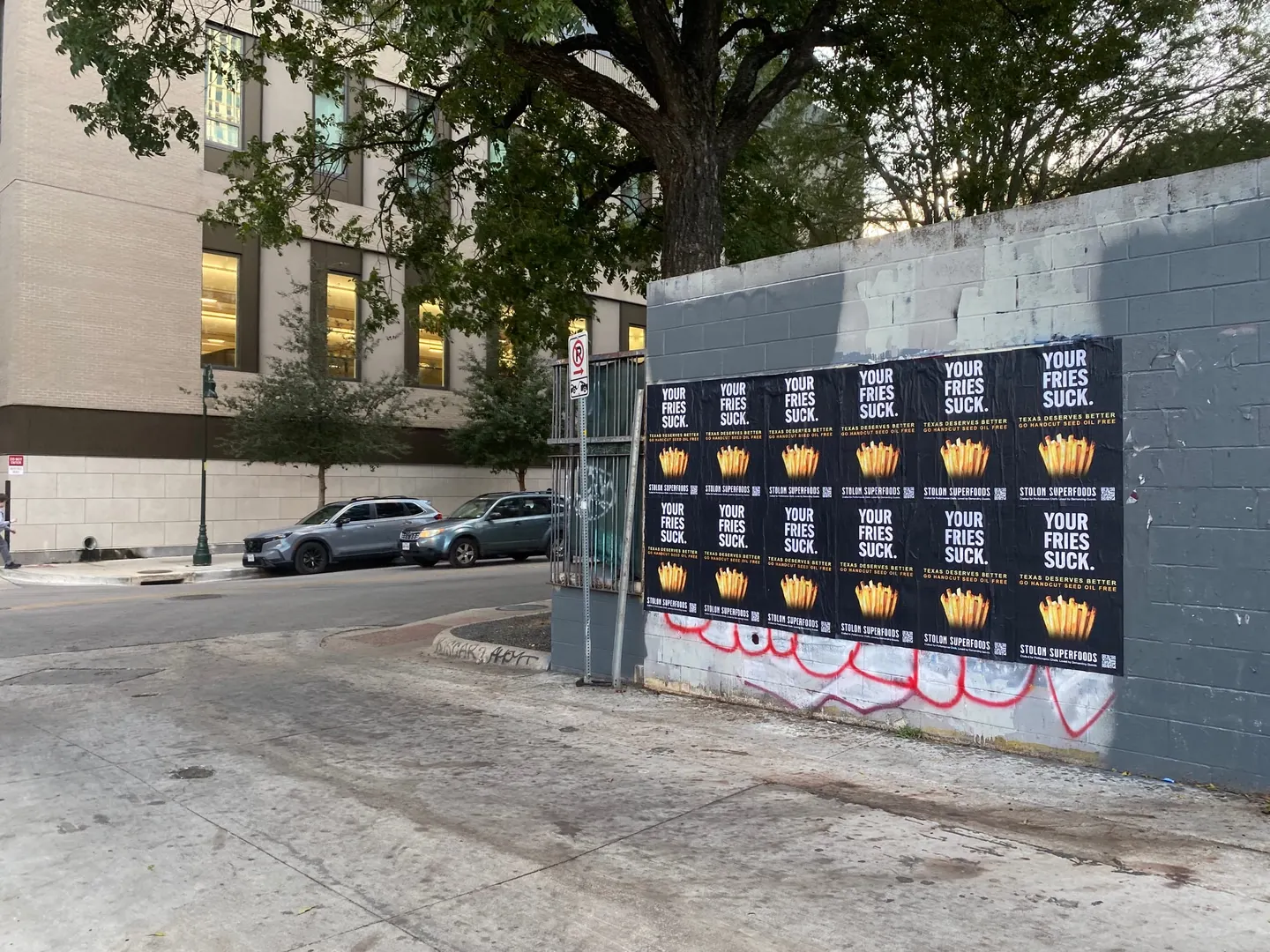 Stolon Superfoods wheatpaste posters, twelve in two rows of six, on grey cinderblock on Guadalupe Street by the UT campus, early evening