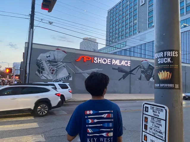Stolon Superfoods pole sticker at a crossing on the Drag, above a START CROSSING placard, a geometric mural across the street, at dusk