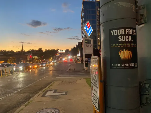 Stolon Superfoods pole sticker on Guadalupe Street by the UT campus, on a thick gray signal pole by a push-button placard, sunset sky behind, at dusk