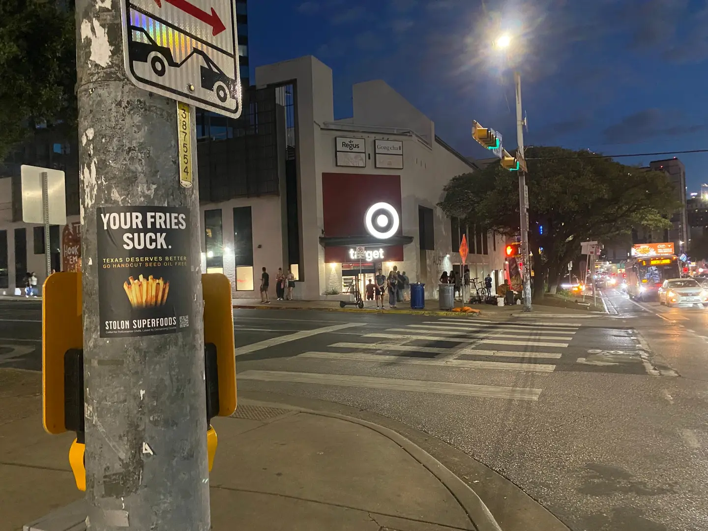 Stolon Superfoods pole sticker on a signal pole on Guadalupe Street by the UT campus, below a tow-away sign at the crosswalk, at dusk