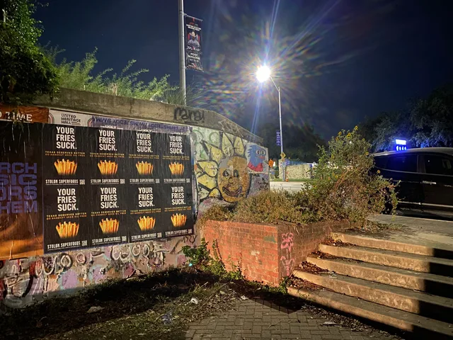 Stolon Superfoods wheatpaste posters, eight in two rows of four, on a graffitied wall by a brick planter on South Congress Avenue, at night