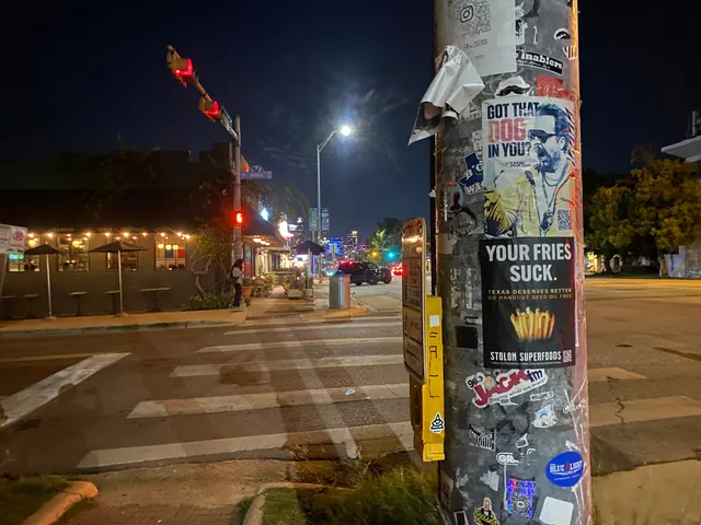 Stolon Superfoods pole sticker on South Congress Avenue, on a heavily stickered pole by a crosswalk and a string-lit patio, at night