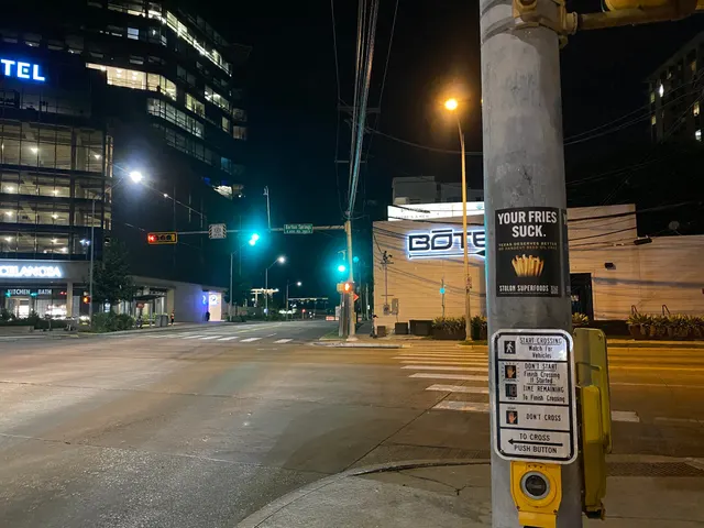Stolon Superfoods pole stickers by Auditorium Shores, two side by side above a push-button placard, the Barton Springs street blade beyond, at night