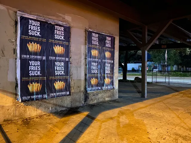 Stolon Superfoods wheatpaste posters, two blocks of four on a concrete wall under an open timber canopy, by Auditorium Shores, at night