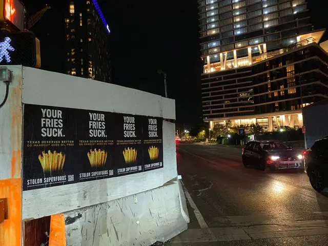 Stolon Superfoods wheatpaste posters, four in a row on plywood above a jersey barrier, on East Cesar Chavez Street near Rainey Street, at night