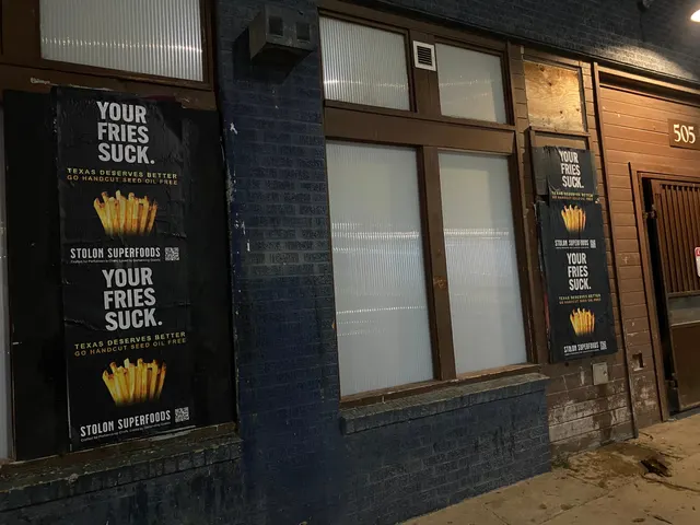 Stolon Superfoods wheatpaste posters, two stacked pairs on boarded windows of a navy and wood storefront, 505, on Red River Street at 7th, at night