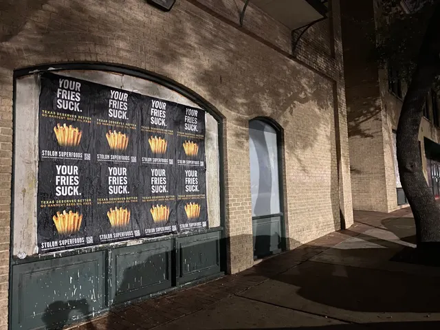 Stolon Superfoods wheatpaste posters in an arched window, tree shadows across the tan brick, on East 6th Street, downtown, at night