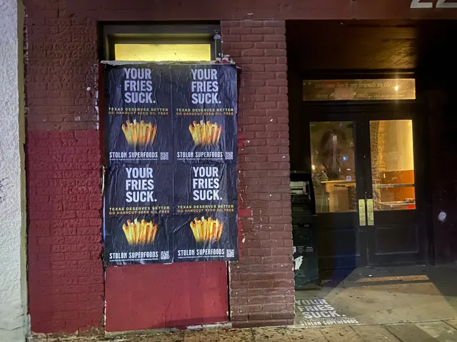 Stolon Superfoods wheatpaste posters, four on red brick, a white chalk stencil by the door, on East 6th Street at San Jacinto, at night