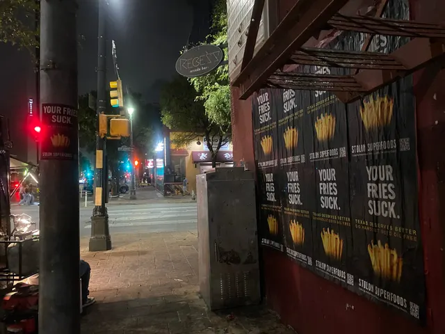 Stolon Superfoods wheatpaste posters, eight on a red wall under a wooden awning, a pole sticker at left, on East 6th Street, downtown, at night