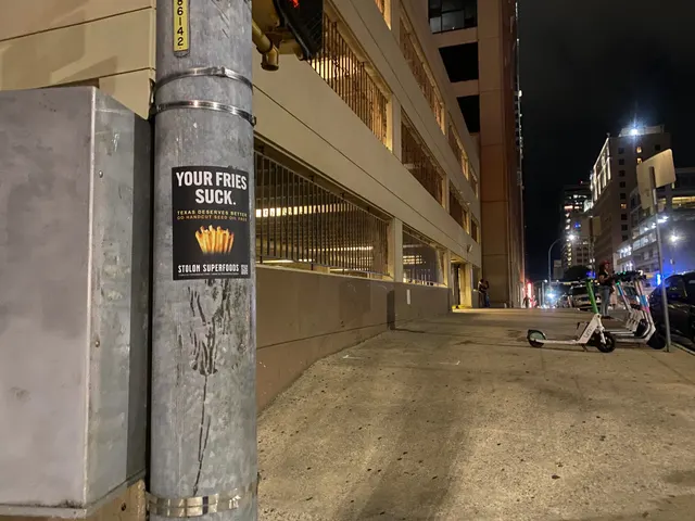Stolon Superfoods pole sticker on East 6th Street, downtown, on a banded galvanized signal pole beside a utility box, parking garage behind, at night
