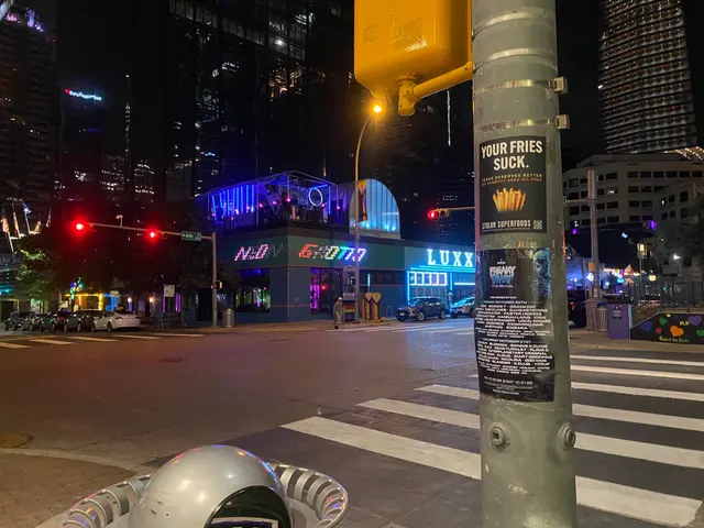 Stolon Superfoods pole sticker on West 4th Street in the Warehouse District, above a festival poster on a signal pole, neon clubs across, at night