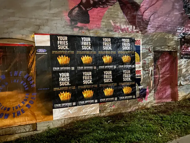 Stolon Superfoods wheatpaste posters centred on muraled brick above a grass strip, on East 6th Street at San Marcos, East Austin, at night