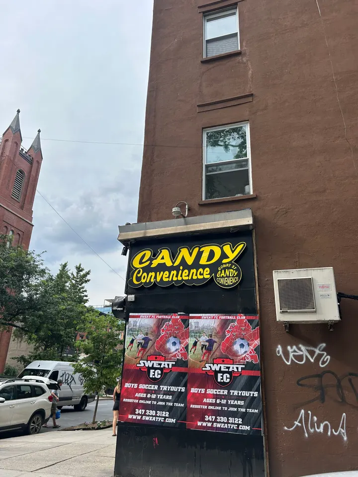 Wheatpaste poster install for Sweat FC youth soccer tryouts on Candy Convenience storefront in Bed-Stuy, Brooklyn, NY, red/black soccer-themed posters with phone number and URL by Beyond Street Media