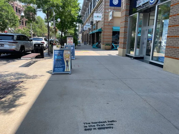 Talk to Strangers sidewalk decal install by Beyond Street Media at 7280 W Alaska Dr, Lakewood, Colorado — a 'The hardest hello is the first one. Say it anyway.' sidewalk decal on a retail walkway.