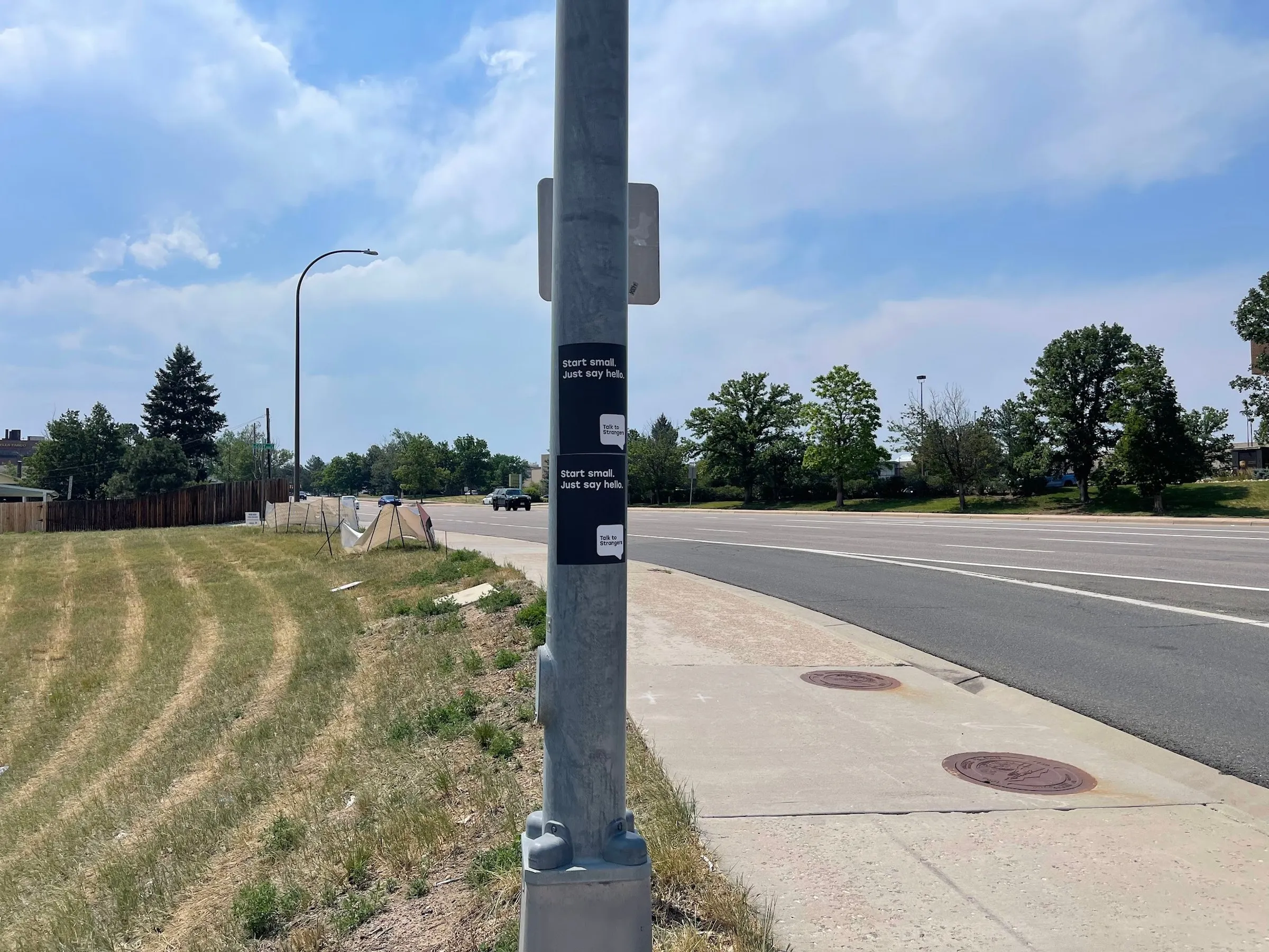Talk to Strangers sidewalk decal install by Beyond Street Media at 5901 S Wadsworth Blvd, Littleton, Colorado — a sidewalk decal on a pedestrian path beside an arterial road.