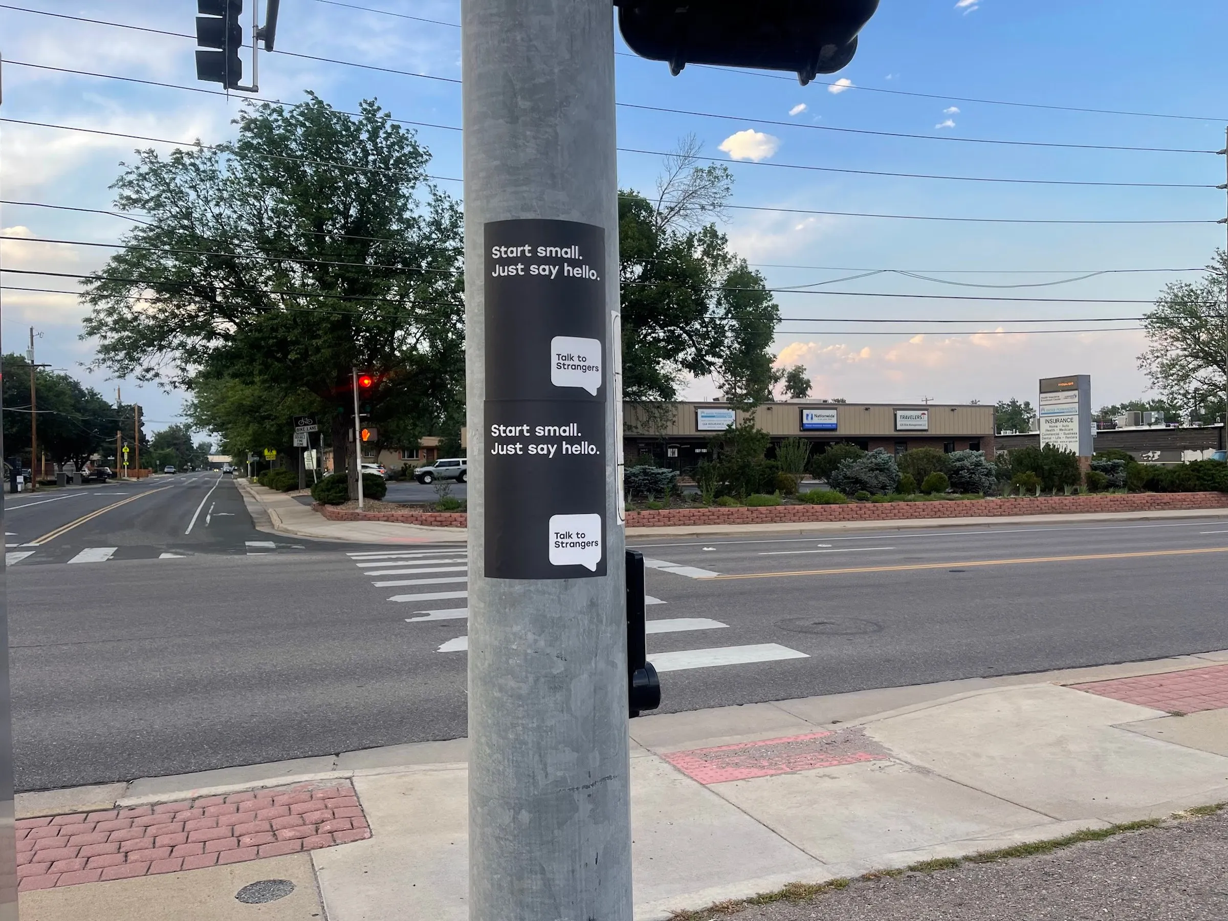 Talk to Strangers pole sticker install by Beyond Street Media at 9195 Co Rd 58, Wheat Ridge, Colorado — a pole sticker at a crosswalk signal on a suburban corridor.